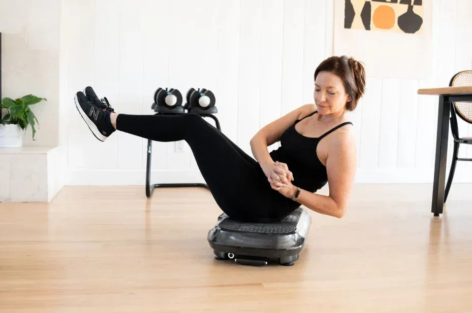 Person holding dumbbells while standing on a vibration plate machine