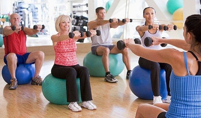 Seniors doing low impact exercise together in a bright community room
