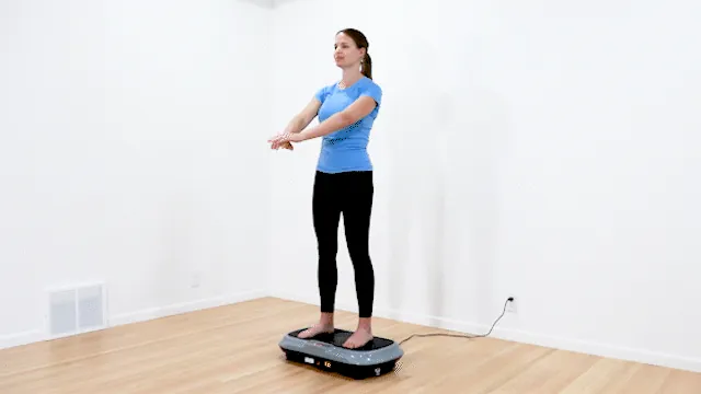 Woman seated on chair with feet on vibration plate in living room.